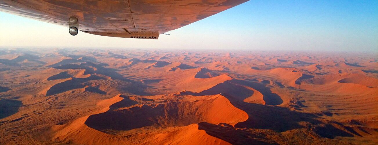 Red sand dunes seen from the air, with the wing of a small aeroplane in view